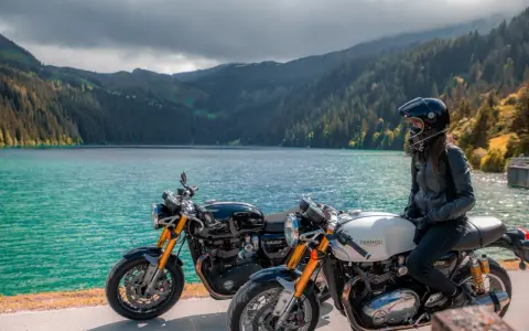 Due moto da enduro, una nera e una bianca, con una donna in sella, godono del panorama di un lago alpino.