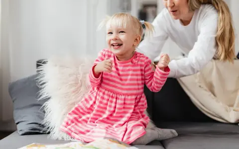 Uśmiechnięta dziewczynka w różowej sukience, która często mówi "kocham cię", bawi się z mamą na kanapie.