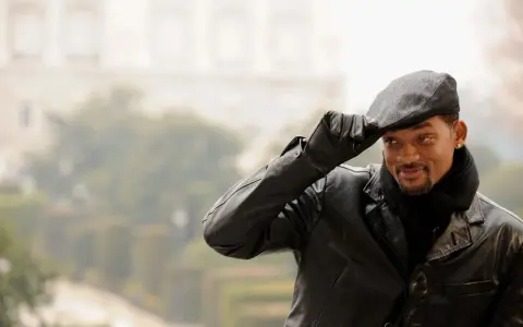 Will Smith, con un berretto uomo, giacca di pelle e sciarpa, saluta con un sorriso.