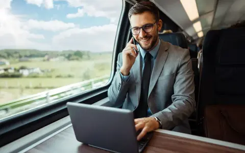 Biznesmen w garniturze rozmawia przez telefon i pracuje na laptopie w pociągu.