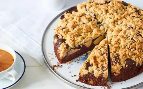 Ein saftiger Apfel Schokoladenkuchen mit knuspriger Streuseldecke, daneben eine Tasse Kaffee.