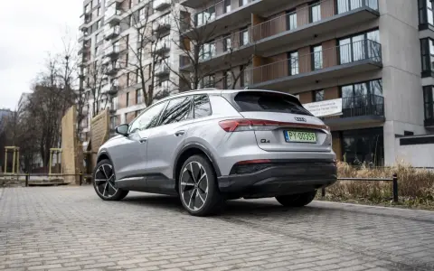 Srebrny Audi Q4 e-tron zaparkowany na brukowanym podjeździe przed nowoczesnym budynkiem mieszkalnym.