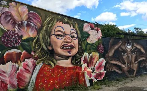 En väggmålning med en busig flicka omgiven av blommor ger graffiti inspiration. Bredvid syns ett mystiskt ansikte med händer.