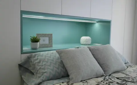 Habitación verde pistacho y gris con cama, almohadas y nicho iluminado.