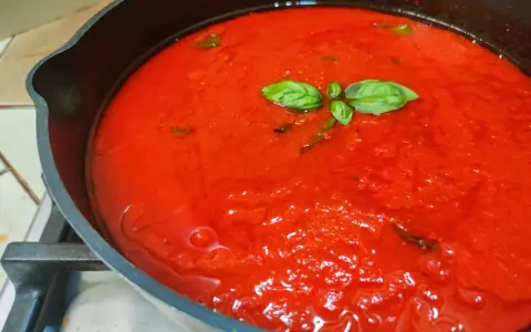 Sugo al pomodoro fresco e profumato, con foglie di basilico che galleggiano in una padella di ghisa.