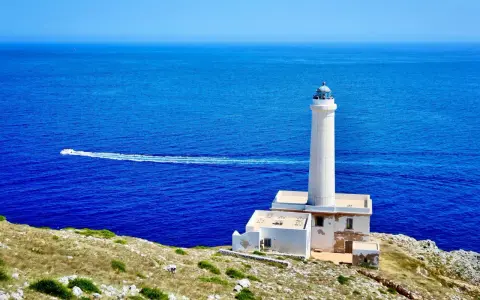 Faro di Punta Palascìa, uno dei luoghi da vedere a Otranto, con il mare blu e una barca in lontananza.