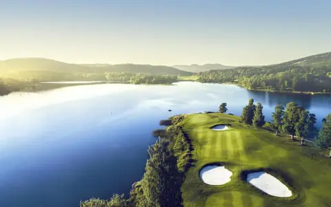 Vacker golfbana vid en sjö, perfekt för norsk golf. Grönskande kullar och solnedgång.