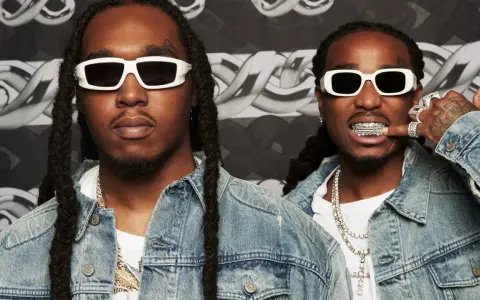 Två medlemmar av Migos, klädda i denimjackor och vita solglasögon, poserar med bling och grillz.