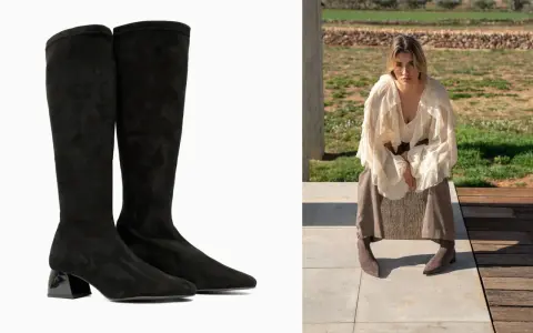 Botas negras de altura de caña con tacón brillante, combinadas con una mujer con falda y blusa voluminosa sentada al aire libre.