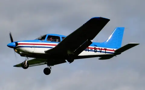 Blau-weiße Piper PA mit roten Streifen fliegt im Himmel.