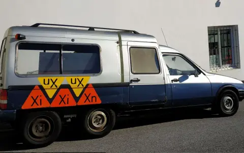 Dwukolorowy Citroen C15 z nietypowymi oznaczeniami "UX" i "Xi Xn" na boku, zaparkowany przy białej ścianie.