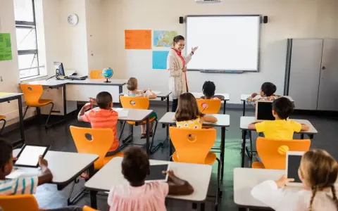 Nauczycielka prowadzi lekcję w klasie pełnej dzieci. To idealne miejsce do nauki pedagogiki przedszkolnej i wczesnoszkolnej w Poznaniu.