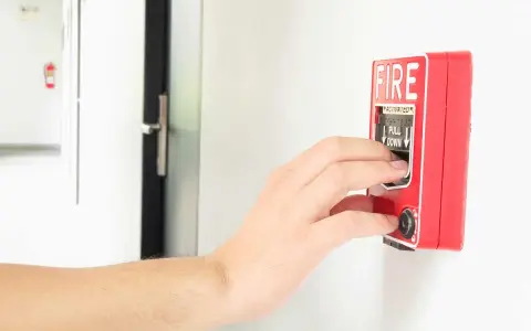 Mano activando la alarma de incendios. Instrucciones claras: "PULL DOWN" para saber cómo apagar alarma de incendios.
