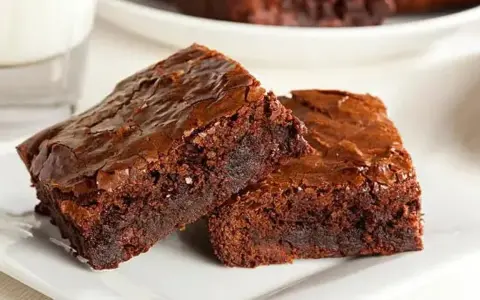 Dos deliciosos trozos de brownie de chocolate, con una textura húmeda y crujiente por encima, listos para ser disfrutados.