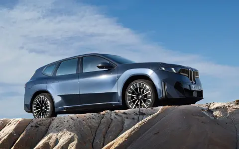 Niebieskie BMW iX3 na tle błękitnego nieba, stojące na skalistym podłożu.