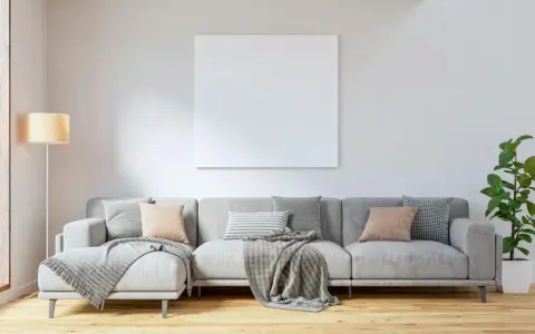 Sofá gris con cojines en tonos tierra y grises, mantas y planta. El color de cojines para sofá gris ideal para un ambiente acogedor.