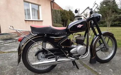 Czarny motocykl z PRL-u, z czerwonym siedzeniem i złotymi ozdobami. Klasyka polskich motocykli.