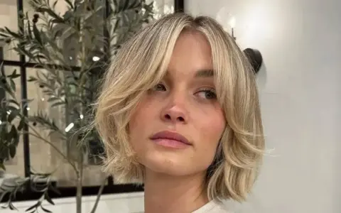 Kobieta z blond włosami w stylu cienkie włosy bob warstwowy cieniowany, z delikatnymi falami i grzywką na bok.