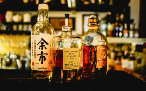 Tre flaskor japansk sprit, inklusive Nikka Whisky From The Barrel och Yoichi, står uppradade på en mörk yta.