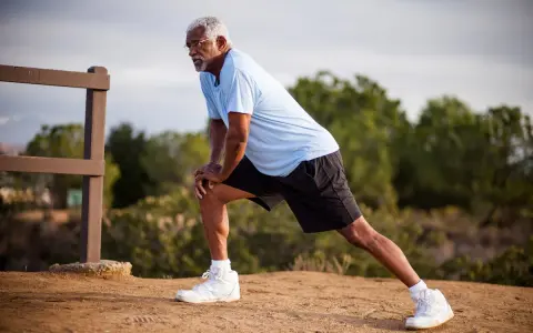 Un homme âgé s'étire pour muscler ses cuisses, un exercice simple en extérieur.