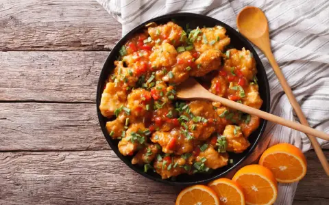 Sabroso pollo a la naranja, cubierto con salsa brillante y cebollín picado, servido con rodajas de naranja fresca.
