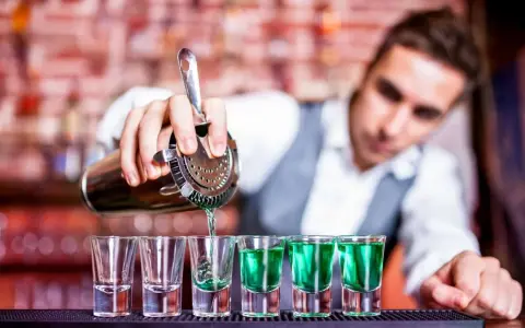 Barman nalewa zielony shot. Zastanawiasz się, ile kosztuje kurs barmana? To inwestycja w przyszłość!