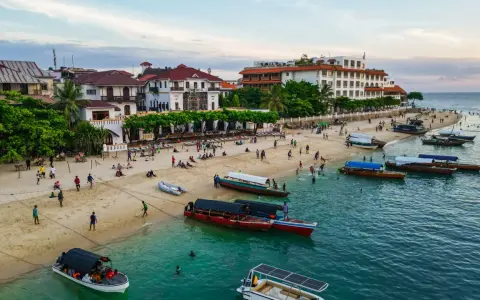 Tanzański szyling na plaży w Stone Town, Zanzibarze. Ludzie odpoczywają, bawią się i pływają, a łodzie czekają na turystów.