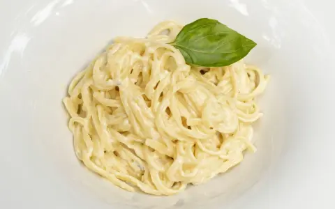 Un plato de spaghetti a la carbonara con nata, cremoso y adornado con una hoja de albahaca fresca.
