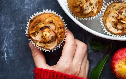 Hand hält einen frisch gebackenen Apfelmuffin, bestreut mit Zimt. Ein tolles Apfelmuffins Rezept!