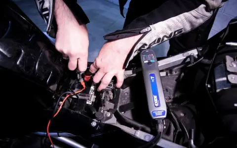 Mani che collegano un caricabatterie Exide alla batteria di una moto, per risolvere il problema della batteria si scarica a moto ferma.