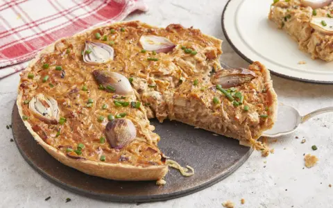 Une délicieuse tarte à l'oignon, garnie d'oignons caramélisés et de ciboulette fraîche, est prête à être dégustée. Une part est servie sur une assiette.