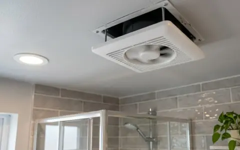 Extractor de baño siempre encendido, ventilando el espacio sobre la ducha. Una luz empotrada ilumina el techo.