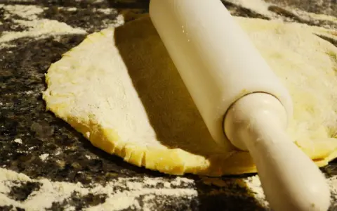 Rouleau à pâtisserie aplatissant une pâte à foncer sur un plan de travail fariné.