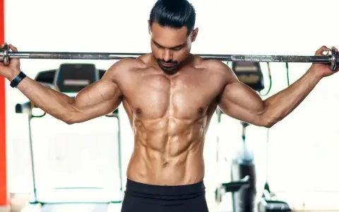 Ein Mann mit stark definierten Bauchmuskeln hält eine Langhantel im **cutten gym**.