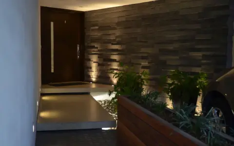 Ingresso con gradino interno illuminato, porta scura, muro in pietra e piante.
