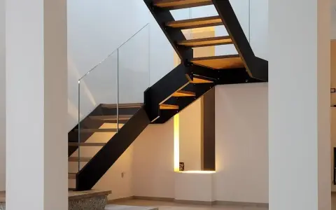 Scala interna con gradini in legno e struttura metallica nera. Il parapetto in vetro trasparente dona leggerezza al design moderno.