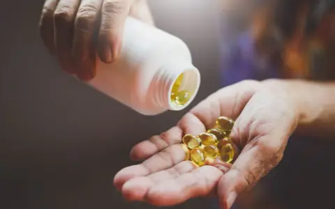 Une main verse des gélules dorées, la vitamine du soleil, dans une autre main.