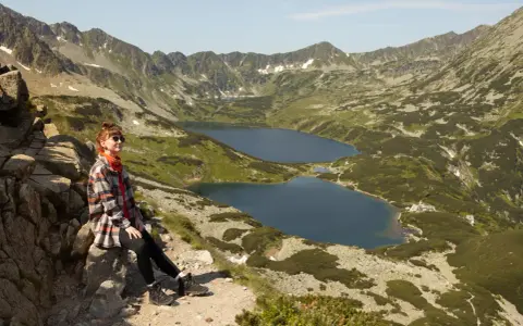 Kobieta odpoczywa na szlaku w Dolinie Pięciu Stawów. W tle rozciągają się góry i jeziora.