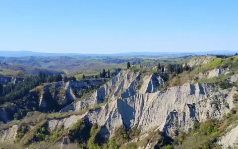 Paesaggio lunare con calanchi toscana, creste erose e vegetazione verdeggiante sotto un cielo azzurro.