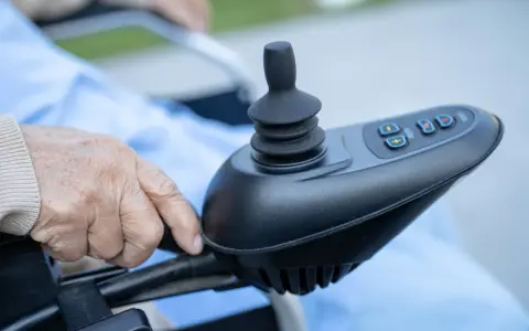 Dłoń starszej osoby na joysticku wózka inwalidzkiego. Czy rozważasz vitafon refundacja NFZ?