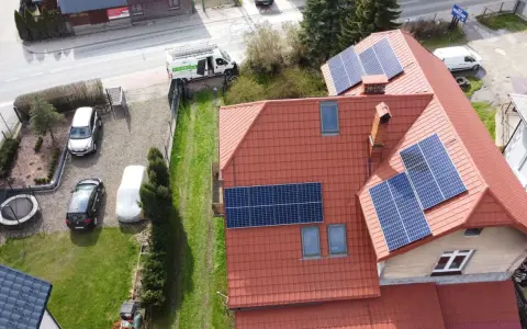 Dachówki i panele fotowoltaiczne na dachu domu. Obok stoi biały van z napisem "FOTOWOLTAIKA".
