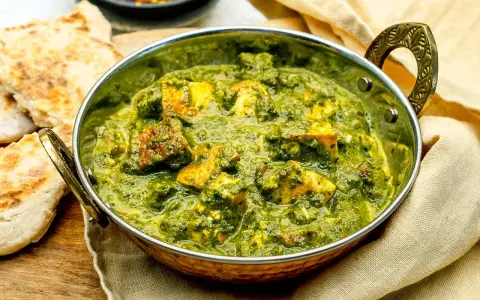 Ein köstliches Palak Paneer in einer Kupferschale, serviert mit Fladenbrot und Chiliflocken.