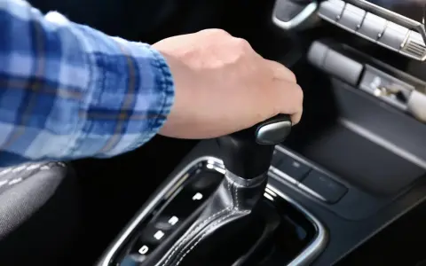 Dłoń na dźwigni zmiany biegów w aucie z funkcją auto hold i manualną skrzynią.
