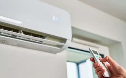 Mano ajustando el aire acondicionado a la temperatura ideal para ahorrar energía. La unidad muestra 21 grados.