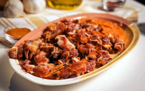 Oreja de cerdo crujiente y dorada servida en un plato con puré naranja.