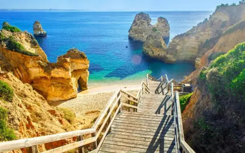 Malownicze schody prowadzą do ukrytej plaży z turkusową wodą, otoczonej klifami. Idealne miejsce na wakacje w portugalskich miastach turystycznych.