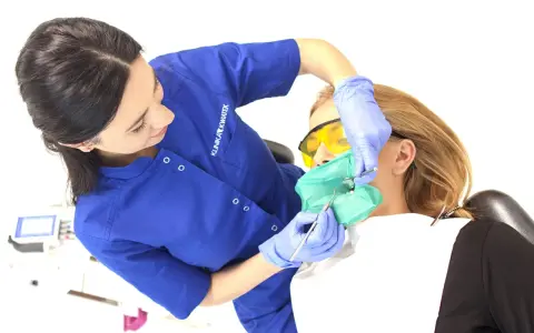 Dentystka zakłada koferdam, zieloną osłonę izolującą ząb pacjentki. To nowoczesne rozwiązanie w stomatologii.