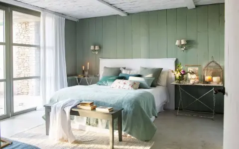 Acogedor dormitorio verde agua y blanco con cama mullida, cojines y luz natural.