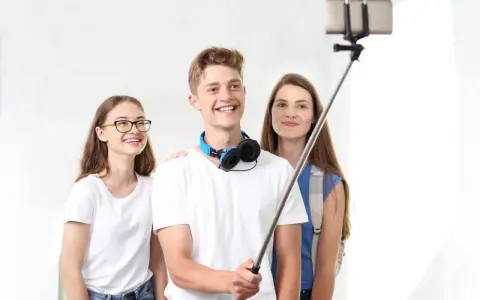 Trzech przyjaciół robi sobie selfie na kijku. Chłopak z przodu uśmiecha się szeroko, pokazując, jak robić zdjęcia.