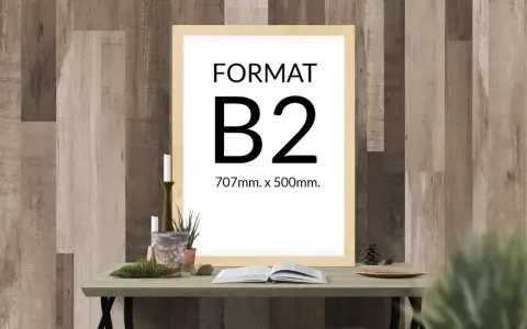 Ramka z napisem "FORMAT B2 707mm. x 500mm." na tle drewnianej ściany. Na stole obok świece, rośliny i otwarta książka.